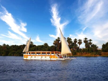 Intimate Nile River Sailing vs Full-Amenity Cruise Ships Traditional wooden sailing vessel gliding past granite islands on the Nile River in Aswan